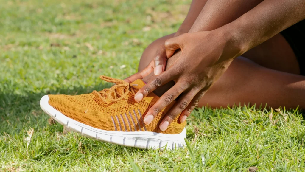 Person holding their foot and ankle in pain after exercise outdoors.