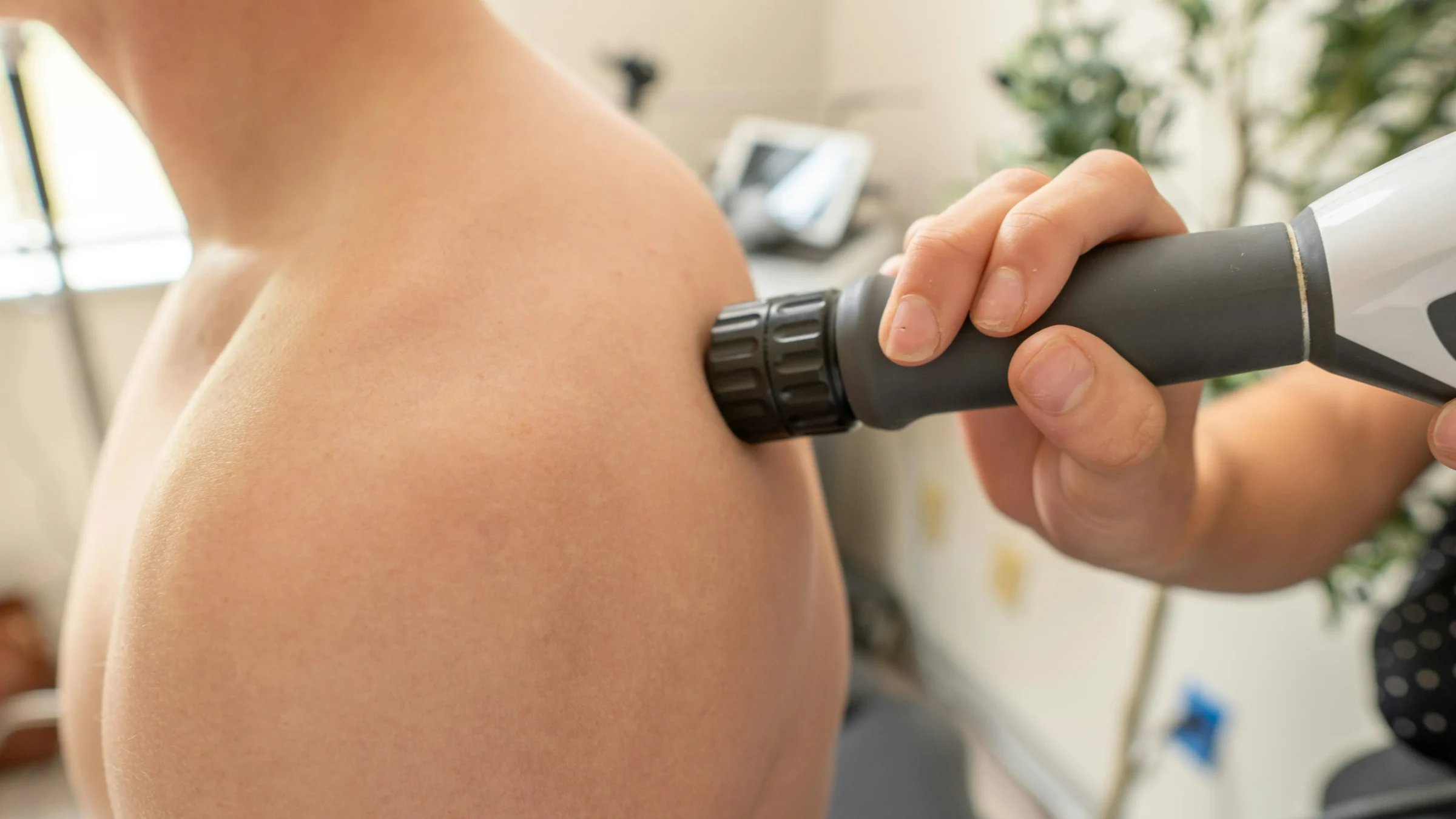 Clinician applying shockwave therapy to a patient's shoulder in a treatment room.
